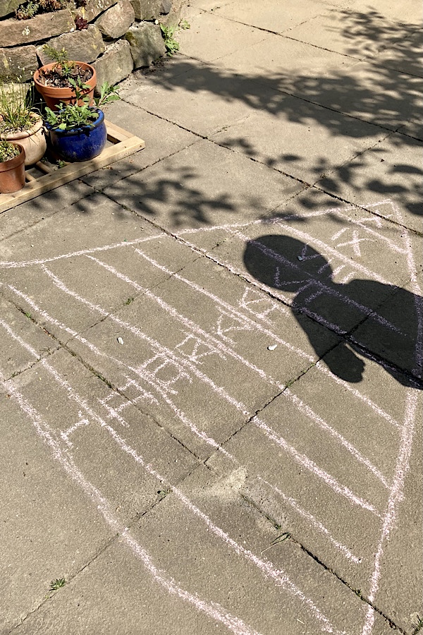 Spielidee im Garten Deltaspiel: Das Bild zeigt ein Dreieck mit einem Meter langen Seiten auf der Terrasse, das in 10 Streifen unterteilt ist, die mit den römischen Zahlen von I bis X beschriftet sind.